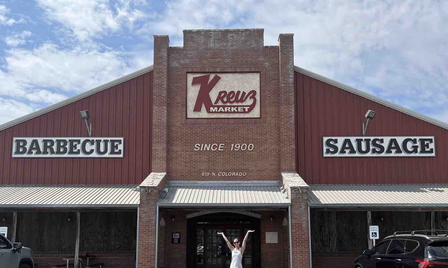 Esther Kho poses in front of a red building featuring a sign that reads 